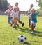 Group of cheerful kids playing football together on green lawn i