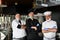 Group chefs standing together in the kitchen at restaurant wearing protective medical mask and gloves in coronavirus new normal