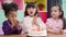 Group of children celebrate birthday`s party in classroom, Multi-ethnic young boys and girls happy make a wish blow out candles o