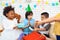 Group of children gives presents to birthday boy in festive hat. Boy is delighted with gifts.