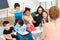 Group of children play a quiz with teacher in peach blouse while in primary school class.