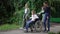 Group of children pushing wheelchair with disabled friend in slow motion outdoors. Smiling positive empathetic Caucasian