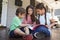 Group Of Children Sit On Porch Of House Reading Books Together