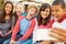 Group Of Children Sitting On Bench In Mall Taking Selfie