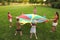 Group of children and teachers playing with rainbow playground parachute on green grass. Summer camp activity