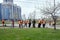 A group of cleaners of bright orange protective vests are sweeping the city sidewalk on a spring street in a residential area