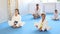 Group of concentrated people, preteen children and adult woman and man, wearing white kimonos sitting on tatami in gym