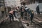 Group of construction workers in work clothes pouring concrete on a building site, with cranes and scaffolding in the background