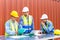 Group of container operators wearing helmets and safety vests meeting about logistics operations in container yards. Colleagues