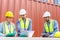 Group of container operators wearing helmets and safety vests meeting about logistics operations in container yards. Colleagues