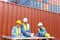 Group of container operators wearing helmets and safety vests meeting about logistics operations in container yards. Colleagues