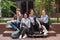 Group of cool smiling students sitting and happily looking in camera while spending time together in courtyard of