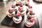 Group of delicious miniature cakes on black serving tray. Forest berries decorated cupcakes. Celebration, party