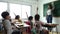 Group of diverse elementary school kids with notebooks sitting in classroom and raise arm up to answer teacher question. Education