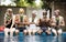 Group of diverse senior adults sitting at poolside holding pineapples together