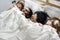 Group of diverse women lying on bed together covered with blanket