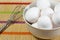 A group of eggs inside a deep white bowl next to a whisk waiting for the chef to use them in a meal on a bamboo mat