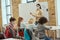 Group of elementary school kids and female teacher wearing protective mask during coronavirus pandemic writing