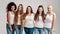 Group of five beautiful diverse young women wearing white shirt and denim jeans smiling at camera while posing together