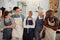 Group of five cheerful diverse clothing designers standing with their arms crossed in a shop at work. Tailors smiling