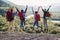 Group of five happy friends jumps at sunset time on background mountains