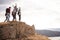 A group of five happy young adult friends cheer with their arms in the air at the summit of a mountain during a hike