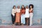 Group of five young happy cheerful businesswomen hugging while standing against a wall outside in the city. Portrait of