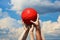 Group of football fans holding red soccer ball in blue cloudy sky. Kid s and adult s hands together hold ball