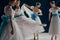Group of four ballerinas, each striking graceful pose in white dresses with blue bows. Elegant dancers in motion.