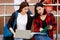 Group of four college student girls holding books and notebook computer sitting and talking together with intimate in front of