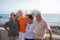 Group of four mature people having fun and talking together at the beach - pensioners seniors smiling and laughing with the sea at