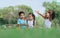 Group of four mixed race African and caucasian little cute kids sitting, playing in outdoor green park for picnic, eating fruit,