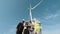 Group of four multiracial coworkers in safety helmets smiling on camera while staning on farm with huge windmills