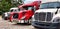 Group of four semi trucks parked on gravel parking lot.