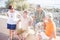 Group of four seniors and mature people together at the beach sitted on a bench or wall and talking - two couples in vacations