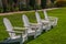 Group of four white Adirondack chairs on green lawn.