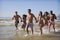 Group Of Friends Run Through Waves Together On Beach Vacation