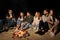 Group of friends sitting at camp fire on beach