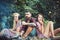 Group of friends sitting next to campfire. Girls leaning on their male friend. Blond woman listening to music while