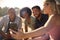 Group Of Friends On Vacation Sitting On Porch Of Countryside Cabin Drinking Beer And Taking Selfie 