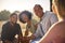 Group Of Friends On Vacation Sitting On Porch Of Countryside Cabin Drinking Beer Together