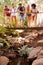 Group Of Friends On Walk Crossing Wooden Bridge In Forest