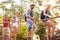 Group Of Friends On Walk Crossing Wooden Bridge In Forest