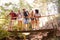 Group Of Friends On Walk Crossing Wooden Bridge In Forest