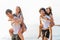 Group of friends walking along the beach, with men giving piggyback ride to girlfriends. Happy young friends enjoying a