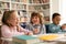 Group of funny diverse international pupils talking and laughing, sitting at table with notebooks and books in classroom