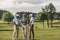 Group of golfers holding clubs and talking while standing on green grass