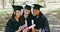 Group of graduates using a phone for social media selfies after graduation ceremony on university campus. Diverse women