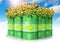 Group of green biofuel drums with sunflowers against blue sky wi