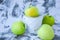 A group of green Granny Smith and golden apples in a white bucket against a white concrete background, copy space for text